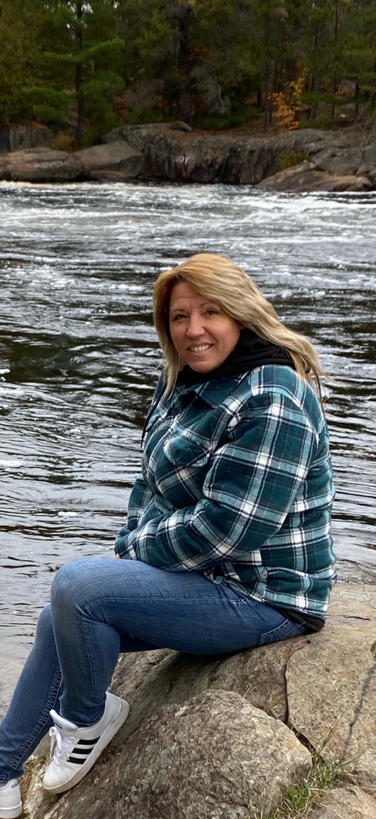 Kimberly Rose sitting on a rock beside an autumn river