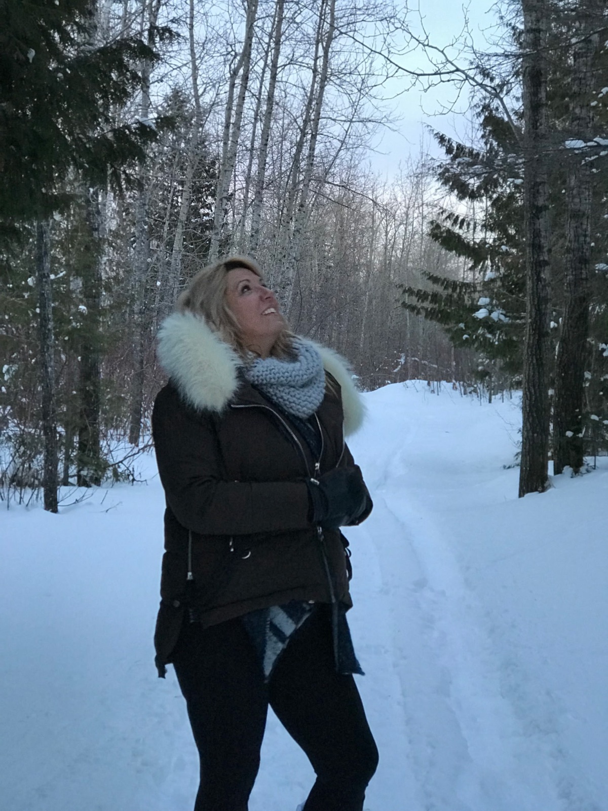 Kimberly Rose on a winter path, looking up toward the trees